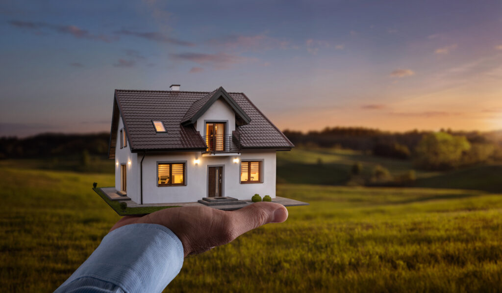 Concept of buying or building new home. Male hand showing, offering a new dream house at the empty field with copy space